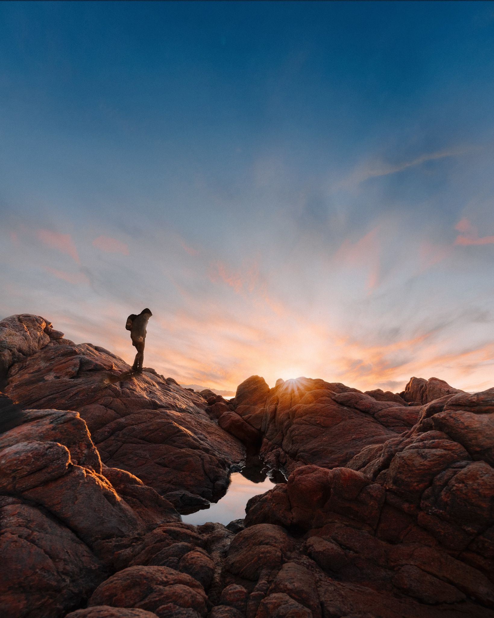 A person walking along a rocky trail at sunset.